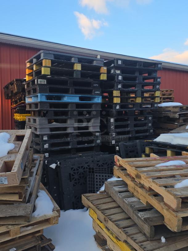 Lot of 4 stacks of black and blue plastic pallets, iGPS brand, used condition, outdoors with visible snow.