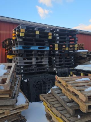 Lot of 4 stacks of black and blue plastic pallets, iGPS brand, used condition, outdoors with visible snow.