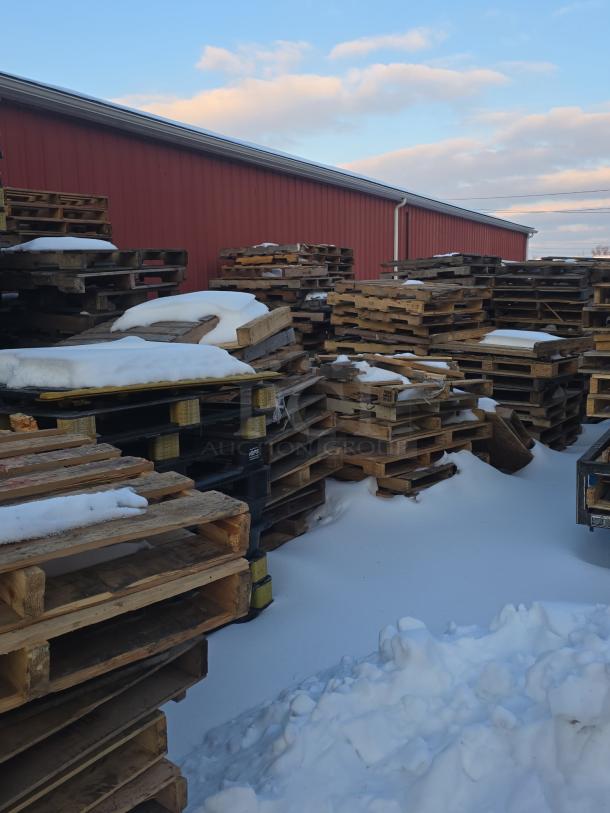 Lot of 10 stacks of wooden pallets, outdoor, some with snow, varying conditions, against a red building background.