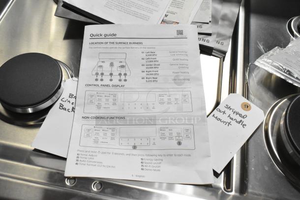 Brand new Samsung gas range with 4 burners, two ovens, missing grates. Includes quick guide. Tags note stripped handle mount.