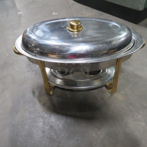 Stainless steel oval chafer with gold accents, includes a lid and sturdy frame, in good condition.