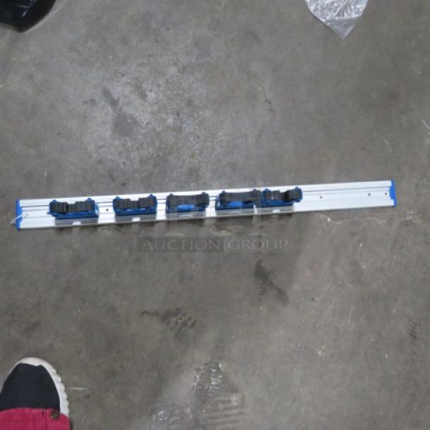 One Unger wall mount mop/broom holder with five adjustable slots, in good condition; ideal for organizing cleaning tools.