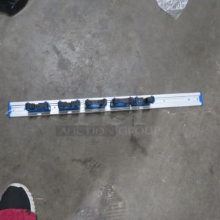 One Unger wall mount mop/broom holder with five adjustable slots, in good condition; ideal for organizing cleaning tools.