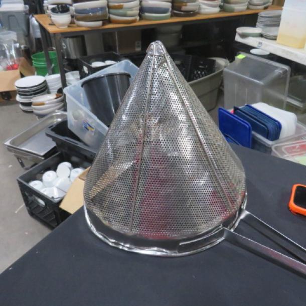 Stainless steel cone strainer with fine mesh, used condition, sitting on a black surface in a kitchen setting.