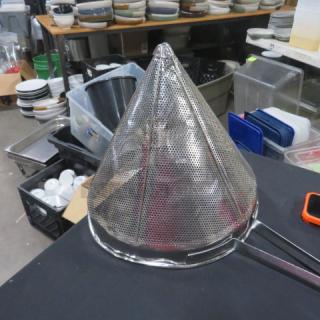 Stainless steel cone strainer with fine mesh, used condition, sitting on a black surface in a kitchen setting.