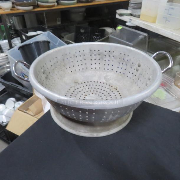 15.5-inch aluminum colander with handles, perforated design. Used condition, suitable for straining and draining.