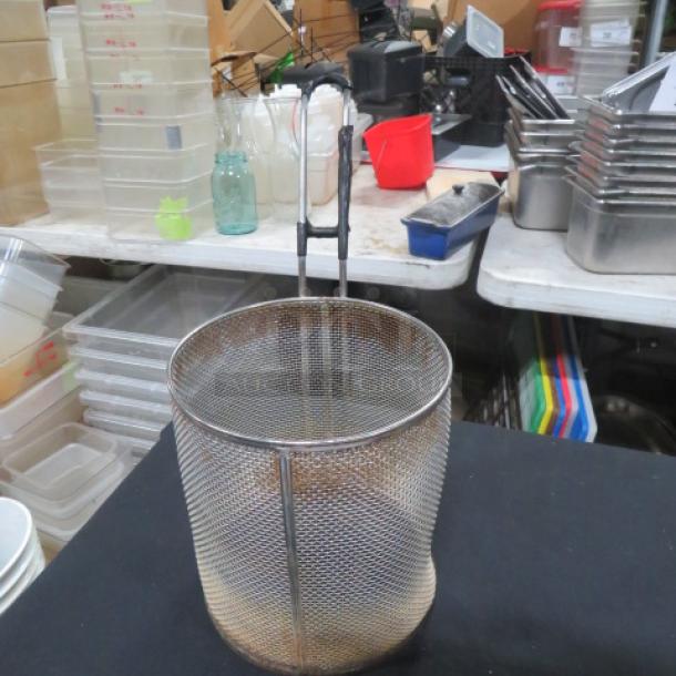 Wire pasta cooker with handle in used condition, set on a table with kitchenware. Ideal for commercial kitchens.