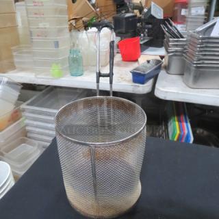 Wire pasta cooker with handle in used condition, set on a table with kitchenware. Ideal for commercial kitchens.