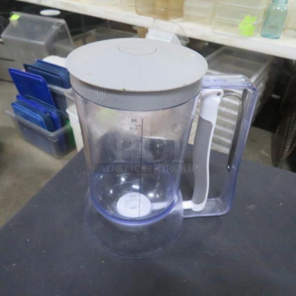 Transparent batter dispenser with white handle and gray lid, marked with ml measurements. Shows minor wear, ideal for precise batter dispensing.