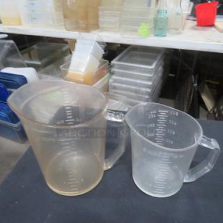 Assorted measuring cups in varied sizes, clear plastic, gradient markings visible, used condition, ideal for kitchen use.