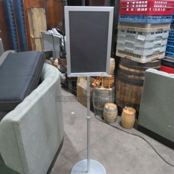 Metal dual-sided sign on stand, silver frame, adjustable height, located in a warehouse setting. Good condition.