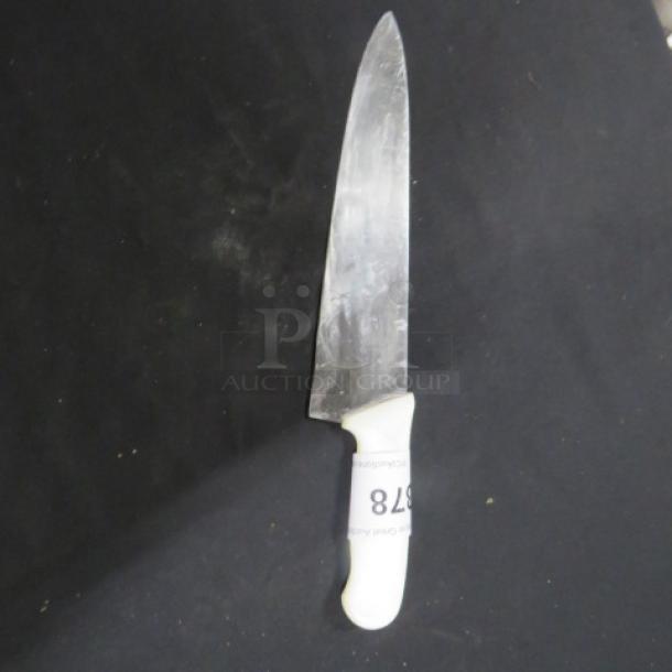 Chef's knife with white handle, visibly used. Blade shows wear. Marked with number 878 for identification.