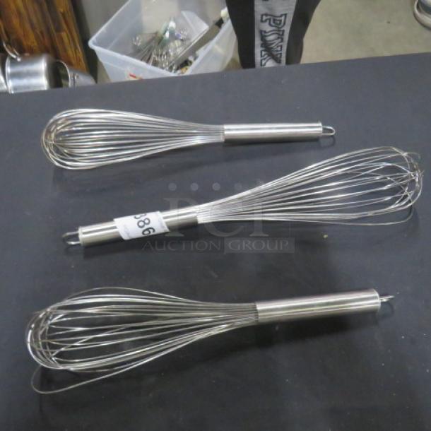 Three stainless steel commercial whisks with loop handles; one marked with tag "986." In good condition.