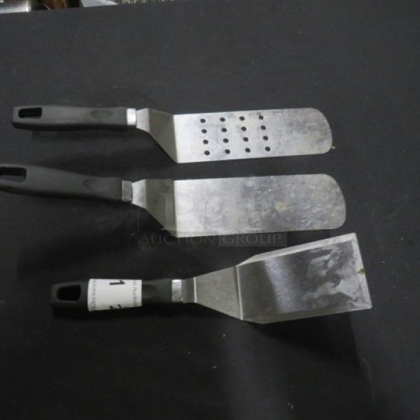 Assorted hamburger turners, set of three, stainless steel with black plastic handles. Includes one perforated turner.