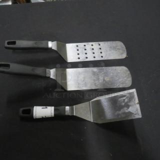 Assorted hamburger turners, set of three, stainless steel with black plastic handles. Includes one perforated turner.