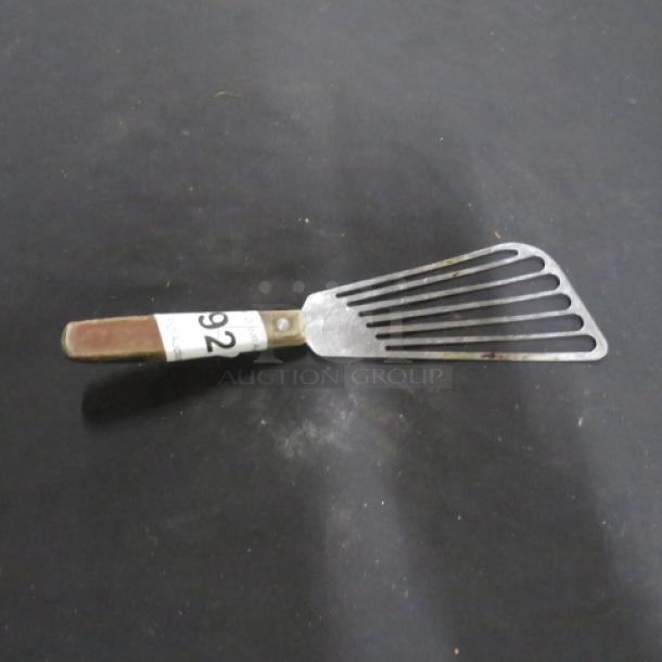 Metal fish turner with slotted blade and wooden handle, item number 92, in used condition.