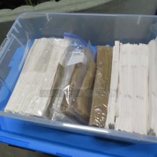 A plastic bin containing assorted white and brown paper bags, some in sealed bags, on a blue surface.