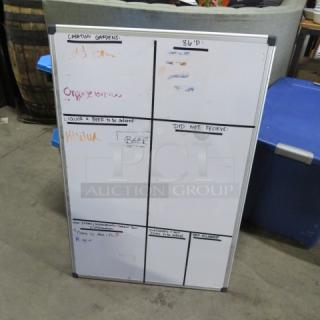 White dry erase board, 24x36 inches, featuring black grid lines and handwritten markings. Good condition with minor wear.