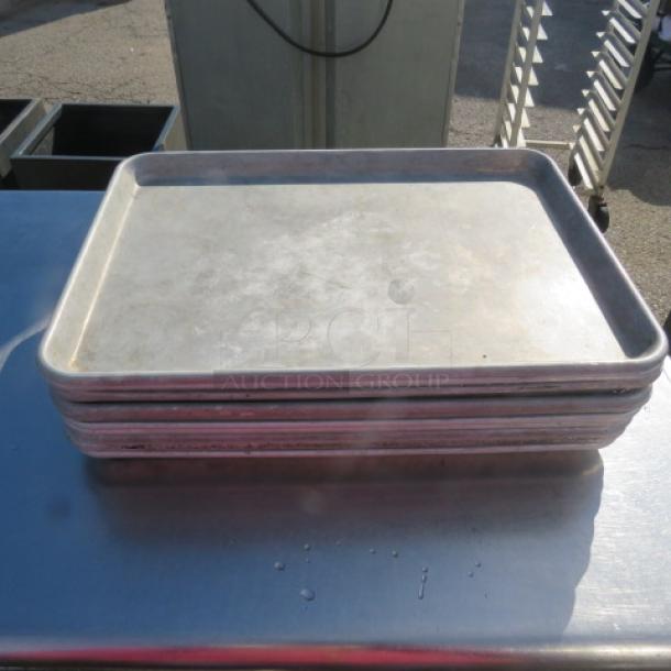 Stack of half size sheet pans in used condition, each with a smooth, worn surface. Ideal for baking and roasting.