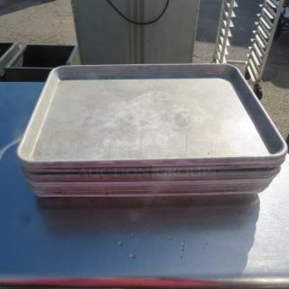 Stack of half-size sheet pans on a metal surface, lightly used. Durable aluminum construction. Ideal for baking or roasting.