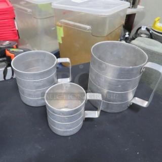 Assorted aluminum measuring cups, set of three, nested design, sturdy handles, visible measurement markings, good condition.