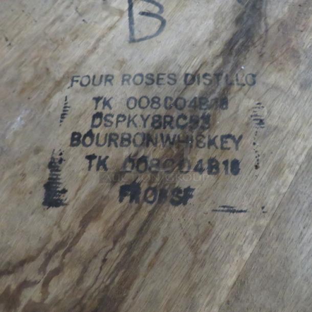 Four Roses whiskey barrel with black markings showing distillery and bourbon whiskey details; rustic condition.