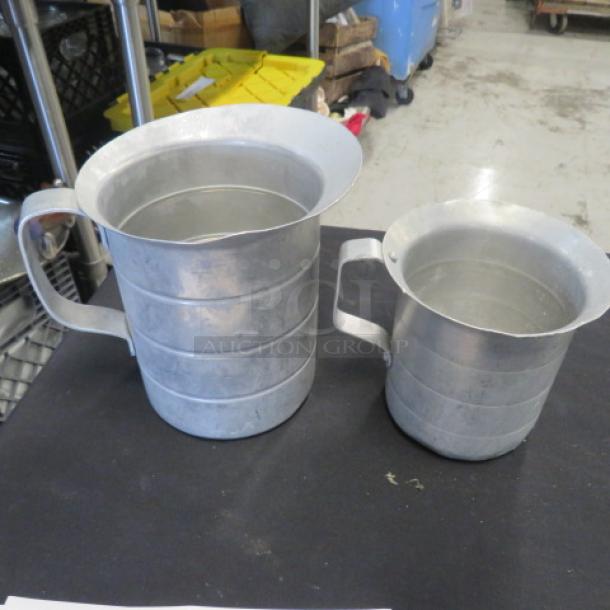 Assorted aluminum measuring pitchers, two sizes, with sturdy handles, in good condition, no labels or markings visible.