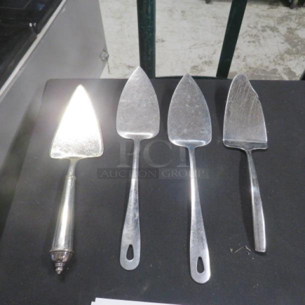 Four assorted pie servers on display; metal, varying handle designs, moderate wear visible, suitable for serving pies.