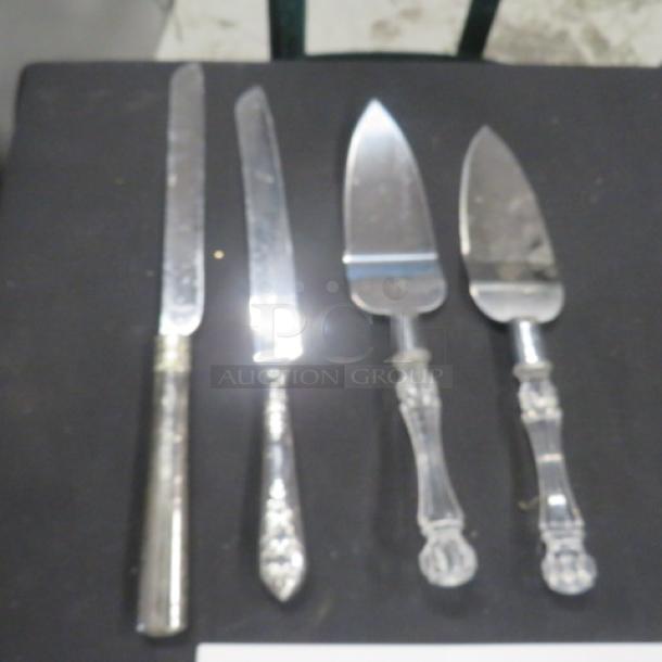 Assorted serving utensils, including two knives and two pie servers, with ornate handles, showing minor wear.