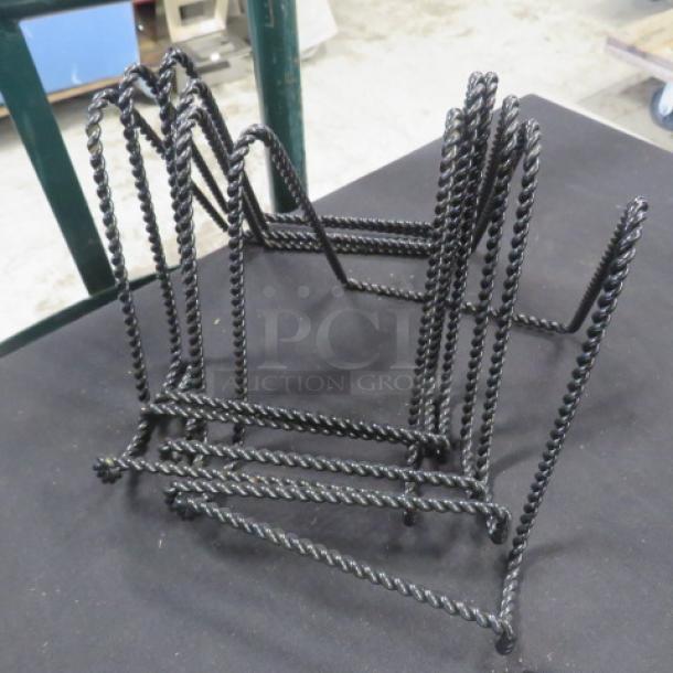 Lot of 6 black metal easels with twisted design; sturdy construction, ideal for displaying plates or artwork.