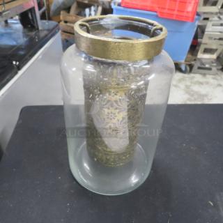 8-inch tall candle holder with intricate brass detailing inside a clear glass jar. Item code: 6XBID.