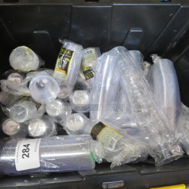 New disposable shot glasses in clear plastic packaging, various stacks in a bin. Each pack labeled with brand details.