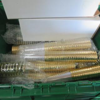 A lot of gold-toned disposable champagne glasses, stacked and wrapped in bubble wrap, in a green bin.