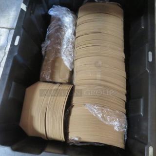 A stack of unassembled paper boats in a large black container, wrapped in plastic. Ideal for craft or display.