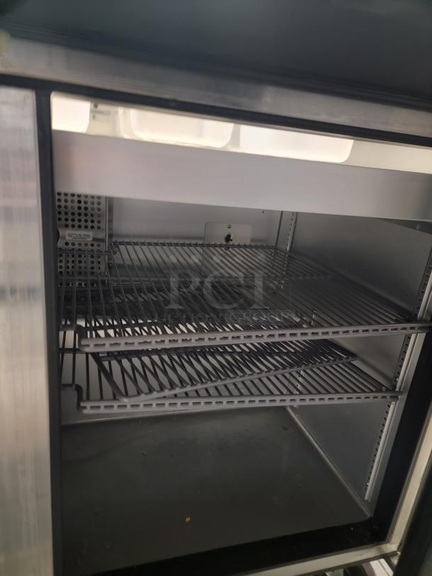 Interior of a True TSSU-48-18M-B-HC sandwich prep table, showcasing spacious wire shelving, stainless steel finish.