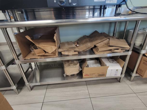 KCS WS-2460 stainless steel prep table with inventory of bulk brown paper bags, drink carriers, and plastic cutlery.