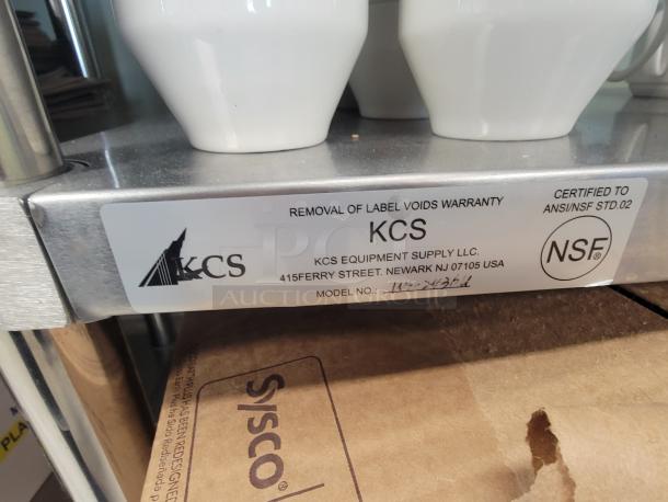 KCS WT-2436 stainless steel work table with NSF certification tag. Visible Sysco paper bags and white ceramic mugs.