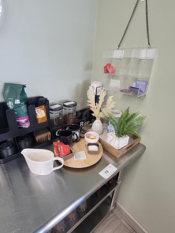 Professional stainless steel coffee & tea station with espresso maker, kettle, Starbucks coffee, Stash tea, mugs, plates, and neon sign.
