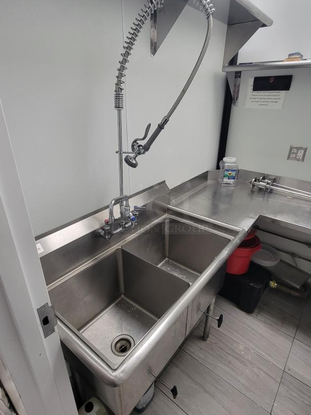 Professional-grade stainless steel commercial kitchen dish station with dual sinks, pre-rinse faucet, and side prep area.