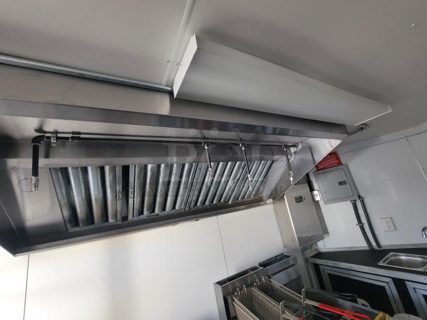 Interior of a 2021 Covered Wagon 16' mobile food trailer featuring a commercial kitchen setup with exhaust hood, fryer, and sink.