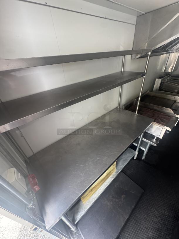Stainless steel prep table with two-tier shelves inside a 2021 Covered Wagon 16' mobile food trailer. Non-slip flooring and ventilation in view.