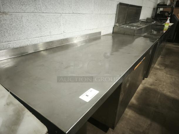 Stainless steel prep table with wooden drawer, good condition, includes back splash; shows auction tag number 8.