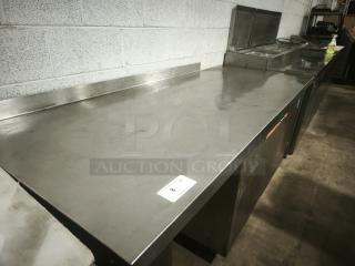 Stainless steel prep table with wooden drawer, good condition, includes back splash; shows auction tag number 8.