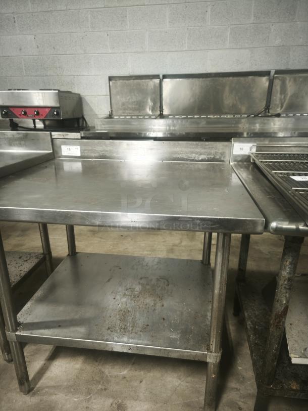 Stainless steel prep table, 36x32x34 inches, showing some surface wear. Features undershelf and backsplash. Ideal for kitchens.