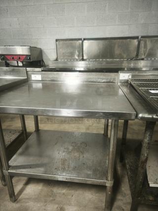 Stainless steel prep table, 36x32x34 inches, showing some surface wear. Features undershelf and backsplash. Ideal for kitchens.