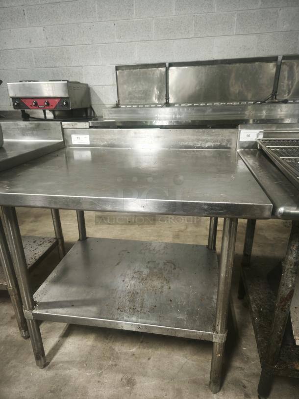 Stainless steel prep table, 36x32x34 inches, with a backsplash and lower shelf, showing signs of wear and use.