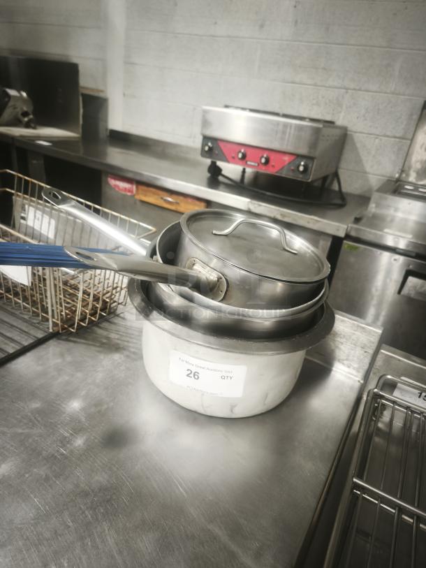 Several stainless-steel saucepans with lids, stacked. Visible labeling indicates auction lot number 26.