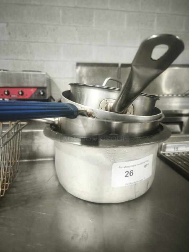 Several stainless-steel saucepans with blue and silver handles stacked, visible auction tag "26," slightly used condition.