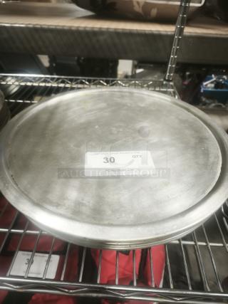 Aluminum pizza pans stacked on a metal rack, showing slight wear. Label indicates quantity of 30 from PCIAuctions.com.