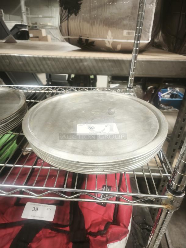 Stack of metal pizza pans on a wire rack, labeled "30 QTY." Light wear visible, indicating prior use.